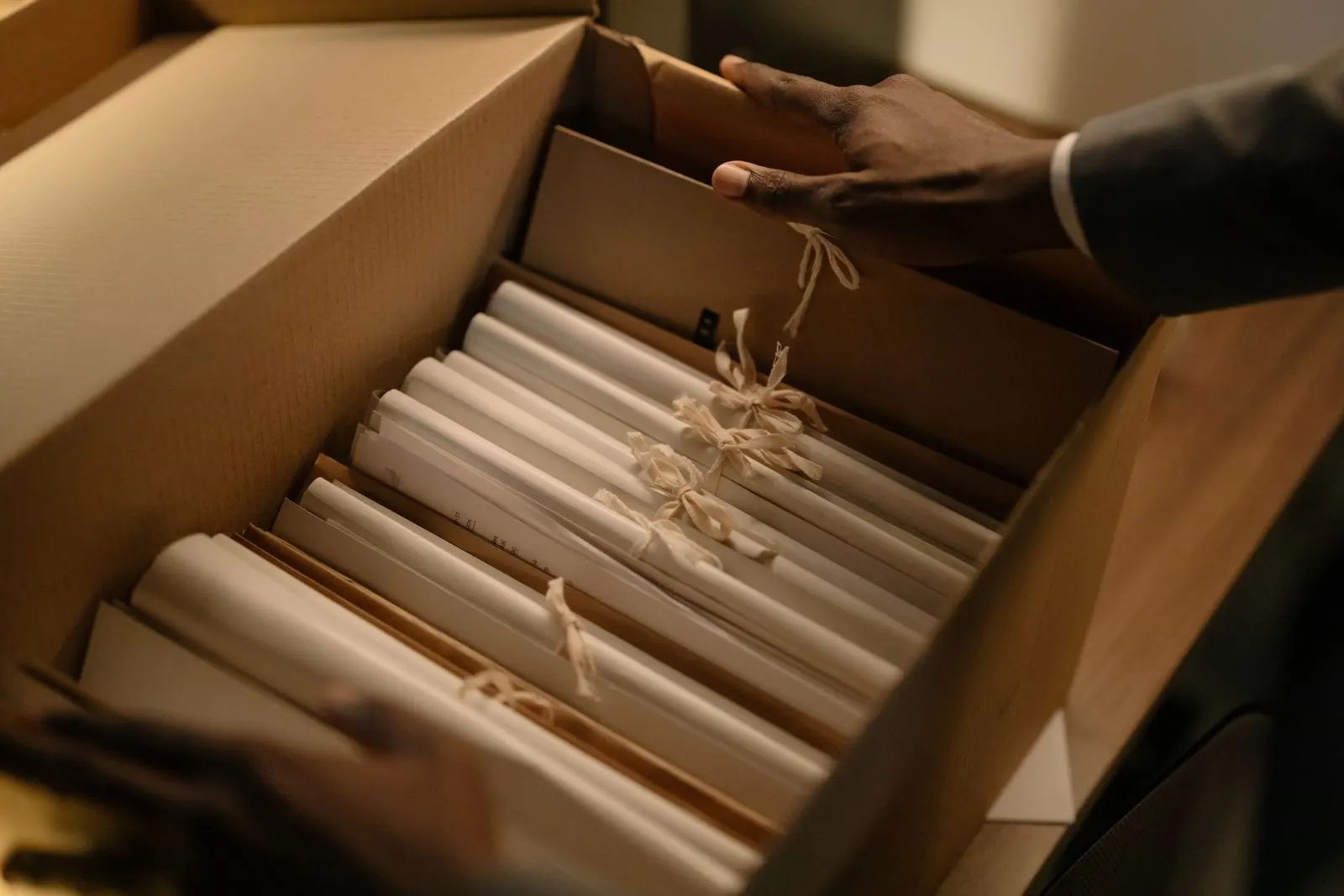 Hände im Anzug durchsuchen eine Archivbox mit verschnürten Aktenbündeln bei der Recherche