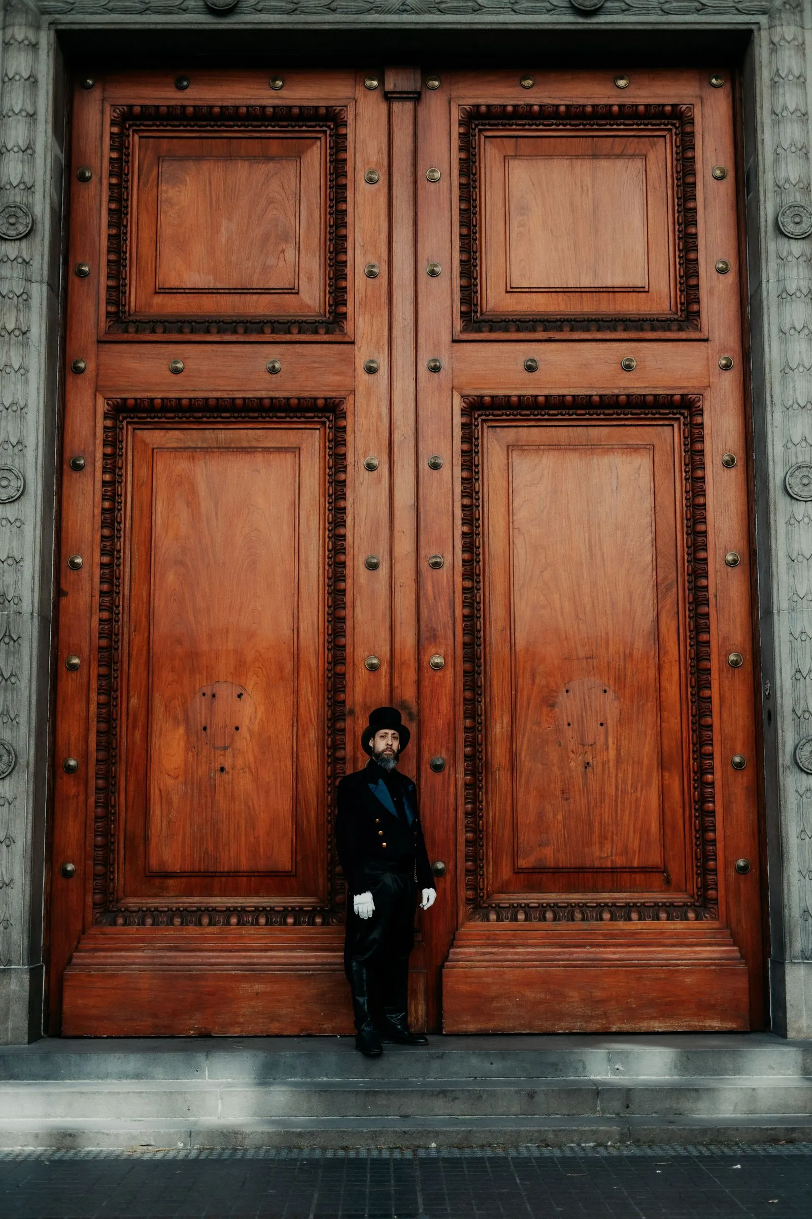 Doorman in eleganter Livree mit Handschuhen vor einem großen historischen Holzportal