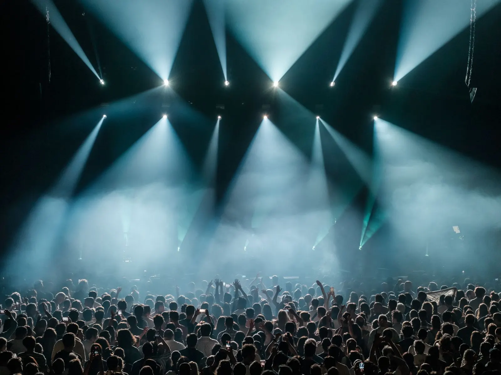 Menschenmenge bei einem Konzert unter blauen Lichtkegeln der Bühnenbeleuchtung