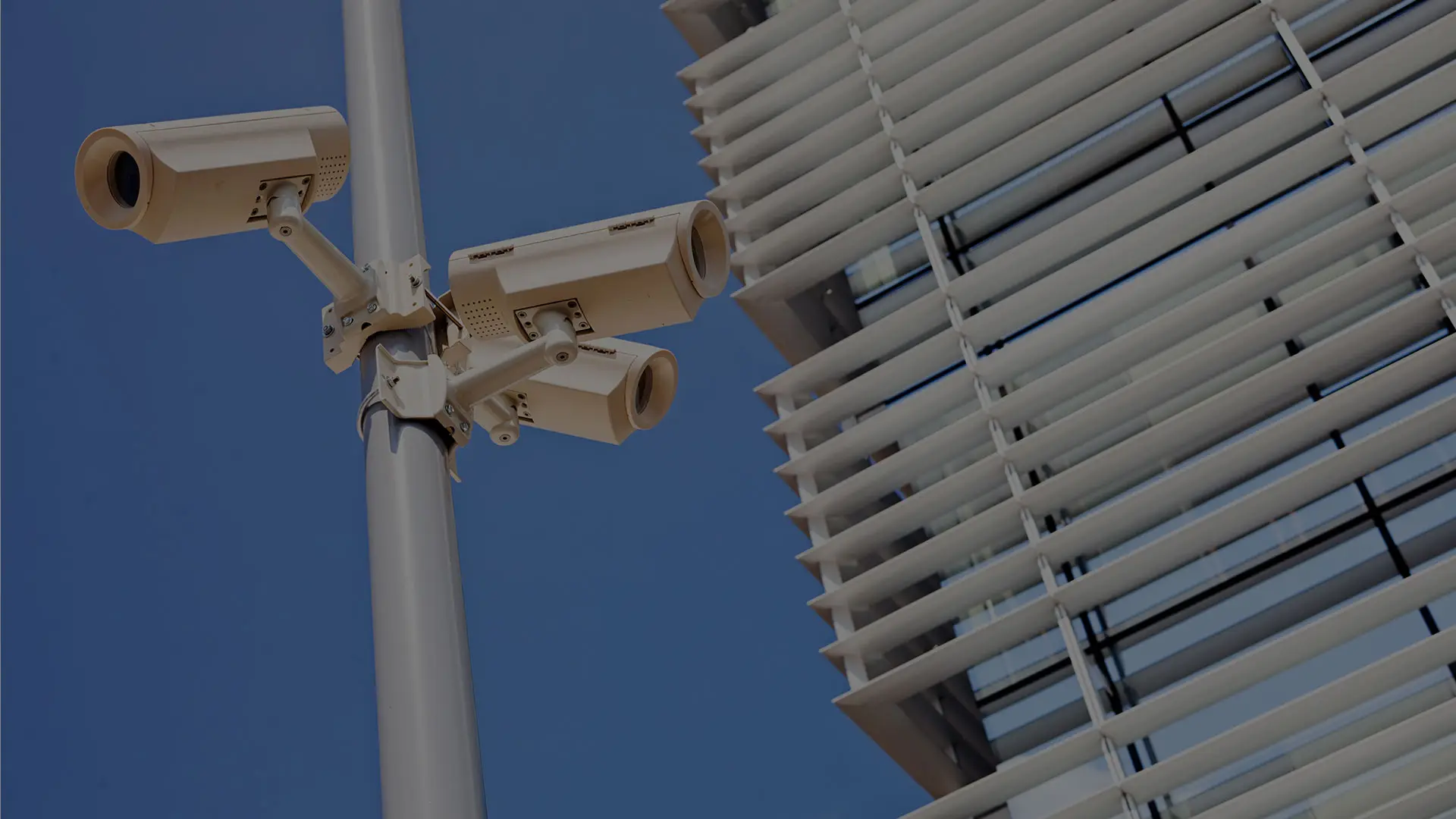 Überwachungskameras an einem Mast vor einer modernen Gebäudefassade