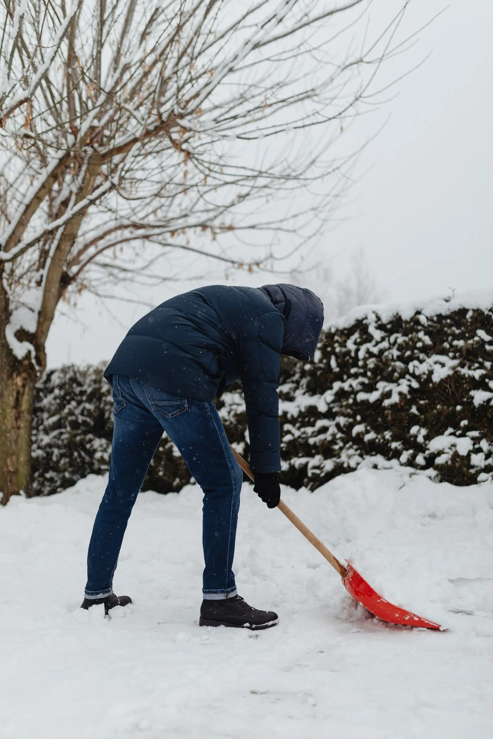 Mitarbeiter räumt mit einem Schneeschieber frisch gefallenen Schnee von einem Gehweg