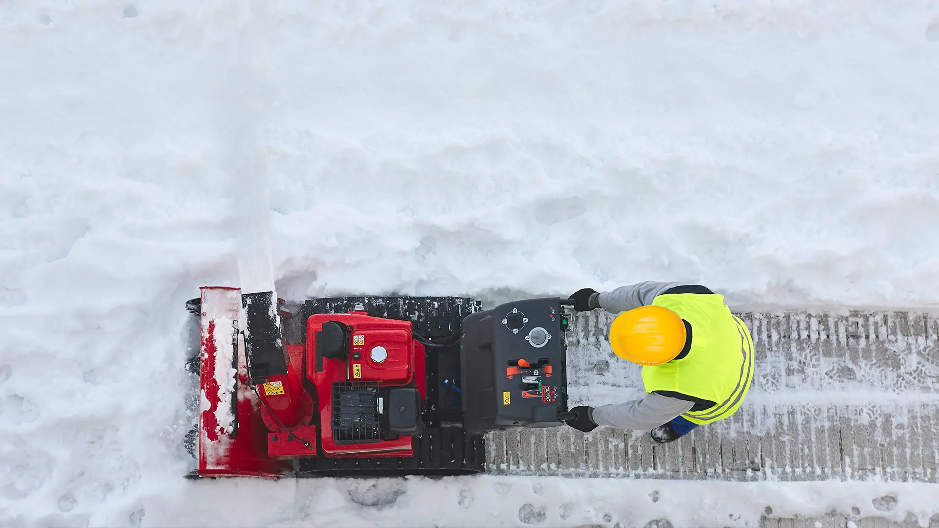 Winterdienst-Mitarbeiter räumt mit Schneefräse einen verschneiten Gehweg